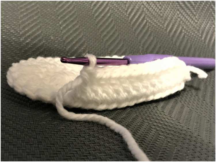 a white crocheted shoe with a purple crochet hook.