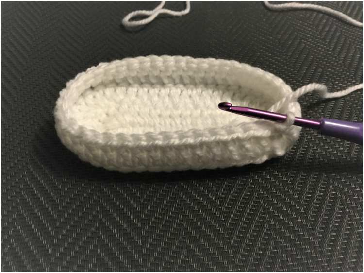 a white crocheted shoe with a purple crochet hook.