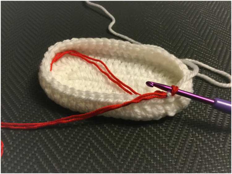 a white crocheted shoe with a red thread.
