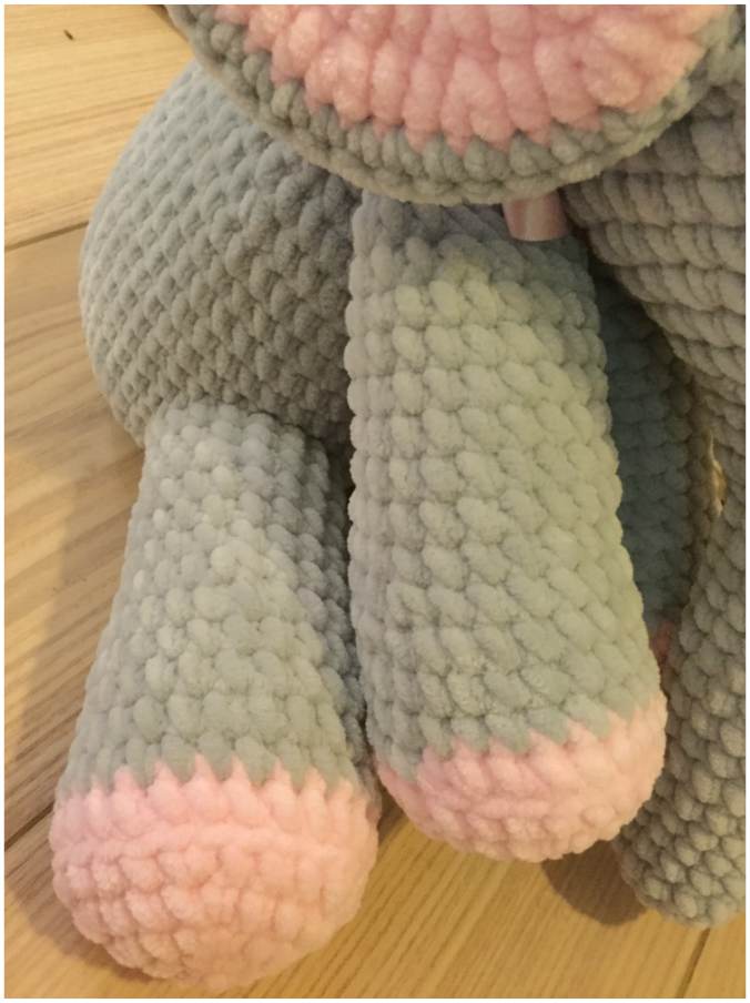 a grey and pink stuffed elephant sitting on a wooden floor.