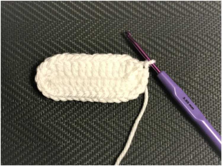 a white crocheted ball is next to a purple crochet hook.