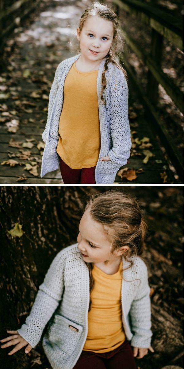 Young child in a yellow shirt and light knit crochet cardigan stands on a wooden path covered with fallen leaves and sits by a tree, looking off to the side.