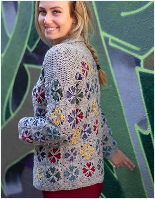 a woman wearing a crocheted jacket in front of a graffiti wall.