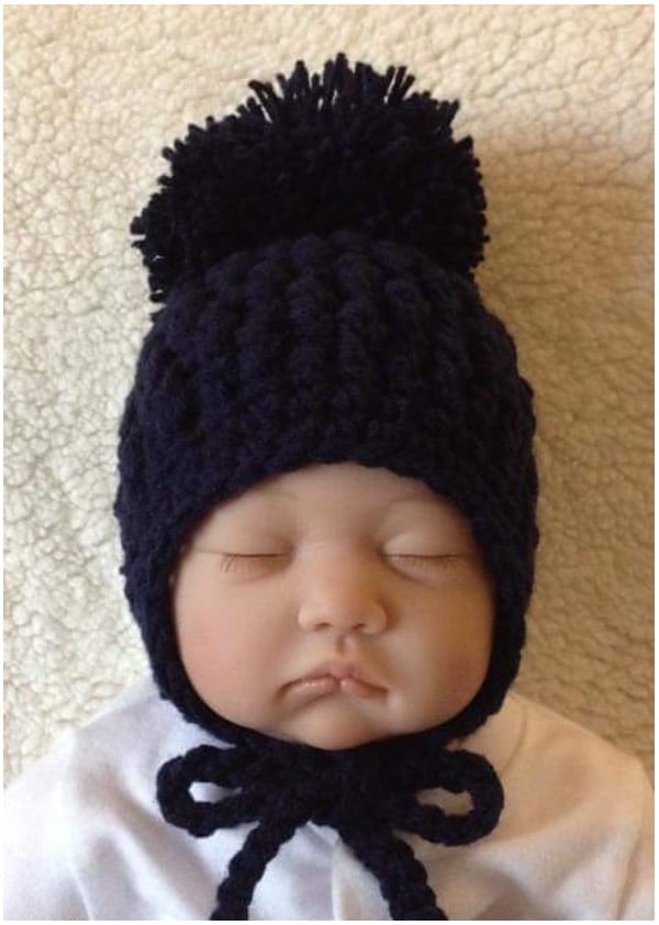 a baby sleeping in a knitted hat with a pom pom.