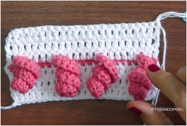 a person is holding a crocheted piece of pink yarn.