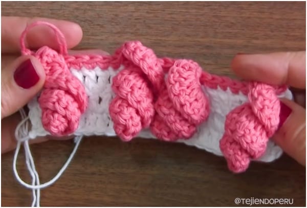 a person is holding a pink crochet stitch.