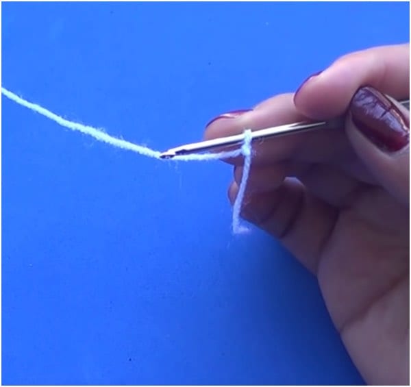 a person is holding a crochet hook to a piece of yarn.