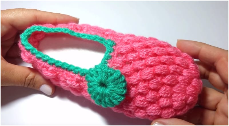 a person holding a pink crocheted baby slipper.