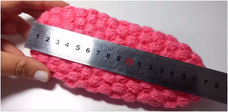 a person is measuring a pink crocheted ball with a ruler.