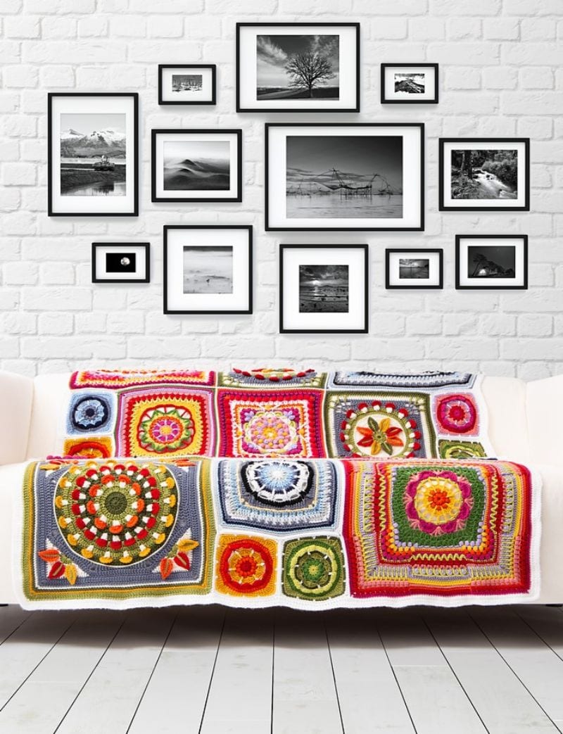 A vibrant crochet throw adorns the white sofa, complemented by a gallery wall of black and white framed photos above.