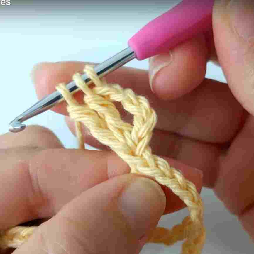 A person is knitting a crochet stitch with a pink crochet hook.