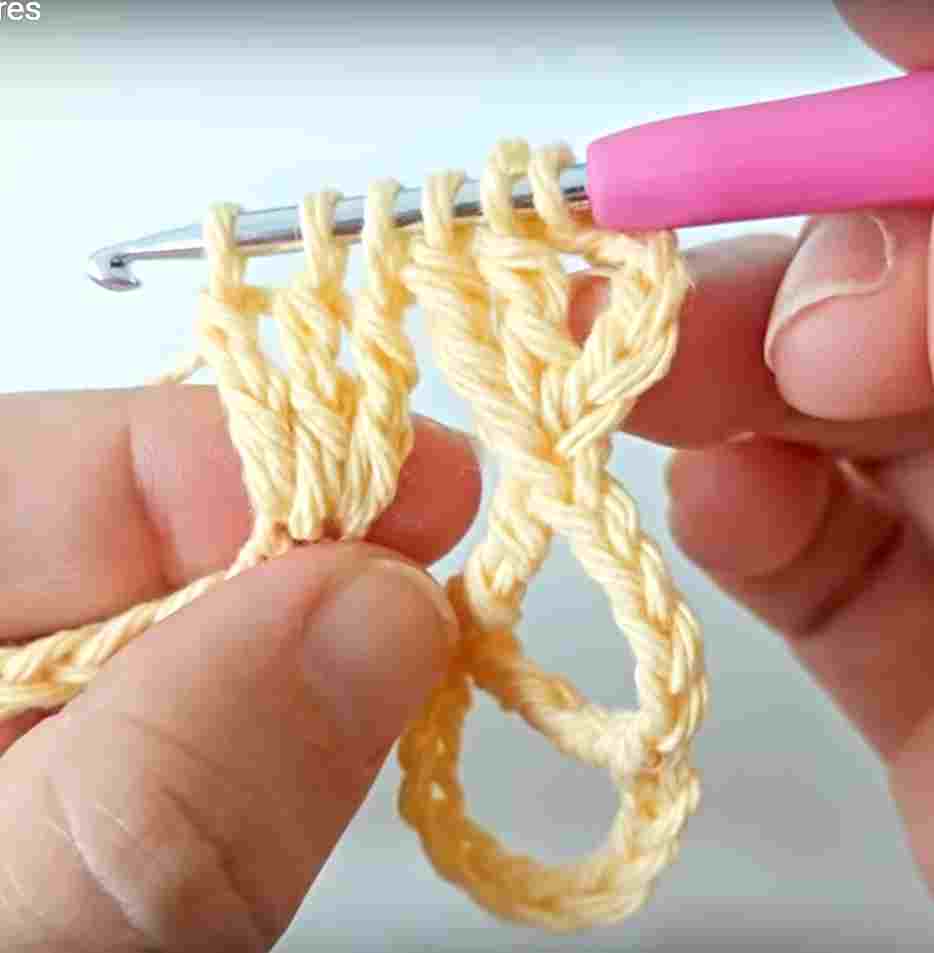 A person is knitting a crochet stitch with a pink crochet hook.