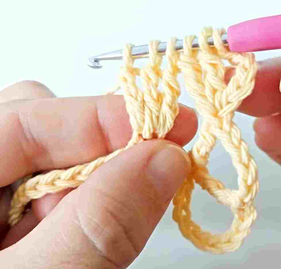 A person is holding a crochet hook to make a crochet stitch.