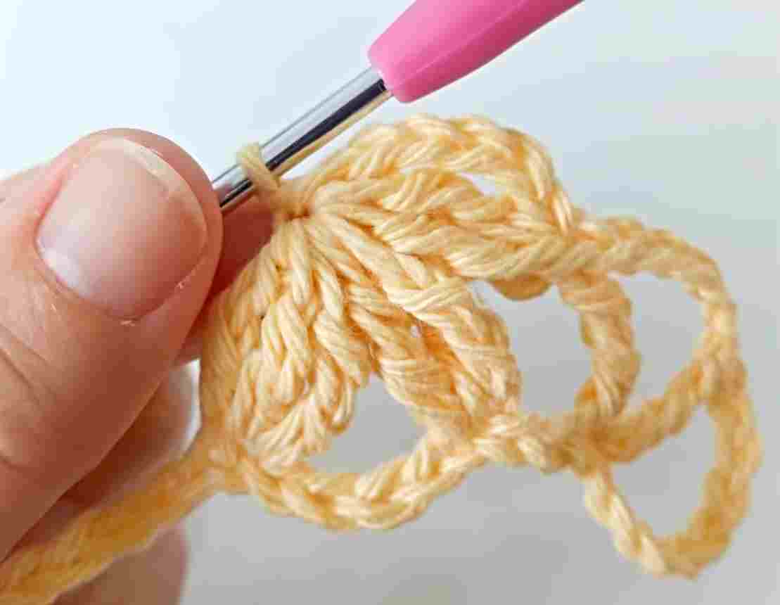 A person is using a pink crochet hook to make a crochet stitch.