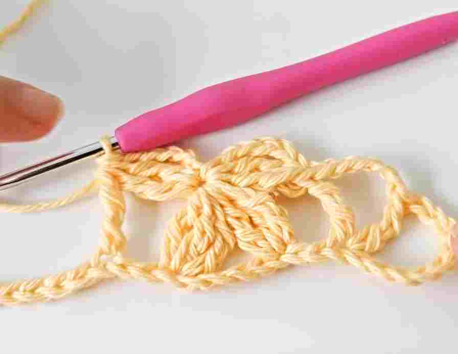 A person is crocheting a bow with a pink crochet hook.