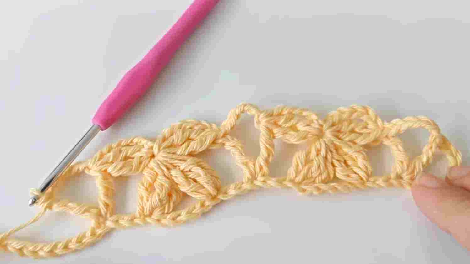 A person is crocheting a bow with a pink crochet hook.