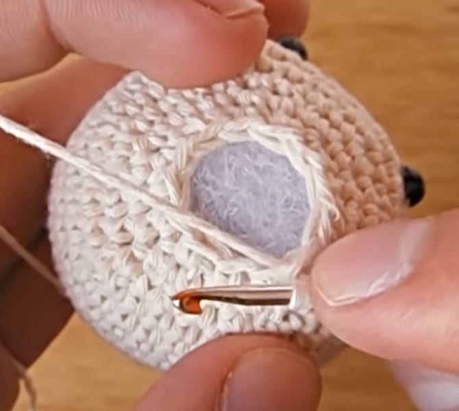 A person is knitting a crocheted ball with a needle.