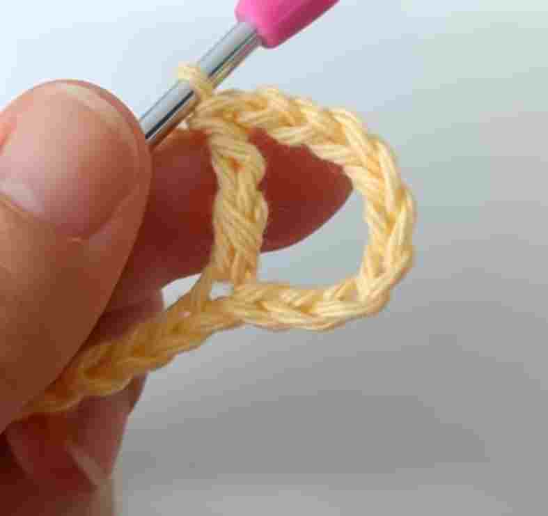A person using a pink crochet hook to make a crochet stitch.