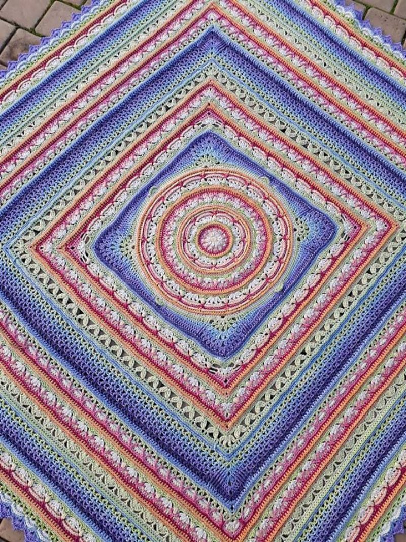 Colorful, intricately crocheted square blanket, this crochet throw features concentric patterns in shades of purple, blue, pink, and green.