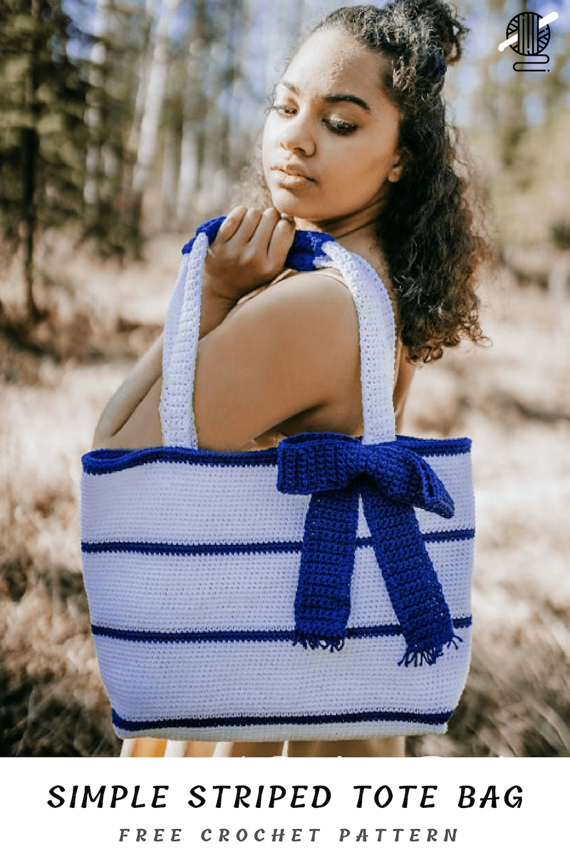 Person holding a stylish crochet bag with white and blue stripes and a bow outdoors. Text reads: "SIMPLE STRIPED TOTE BAG FREE CROCHET PATTERN.