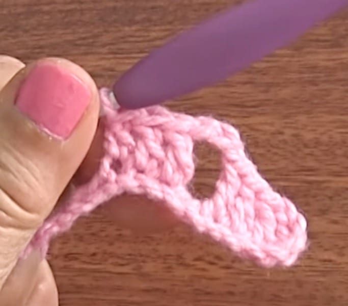 A person is using a pink crochet hook to make a hole.