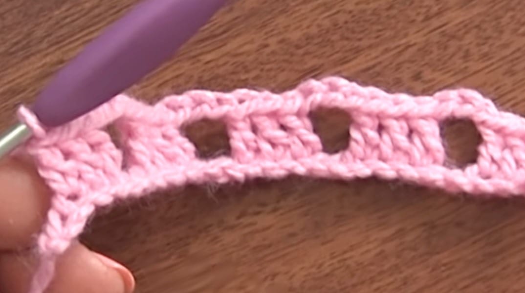 A person is crocheting a pink crochet stitch.