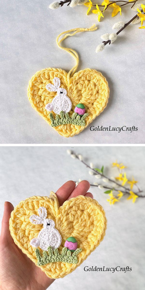 A handcrafted crochet heart with a small white bunny and colorful accents, including crochet Easter eggs, displayed against a gray background, with a glimpse of yellow flowers.