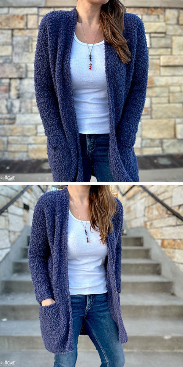 Woman wearing a long crochet cardigan, white top, and jeans standing against a stone wall.