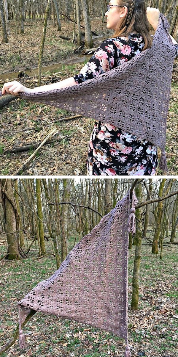 A person displays a triangular, crocheted shawl outdoors in a wooded area.
