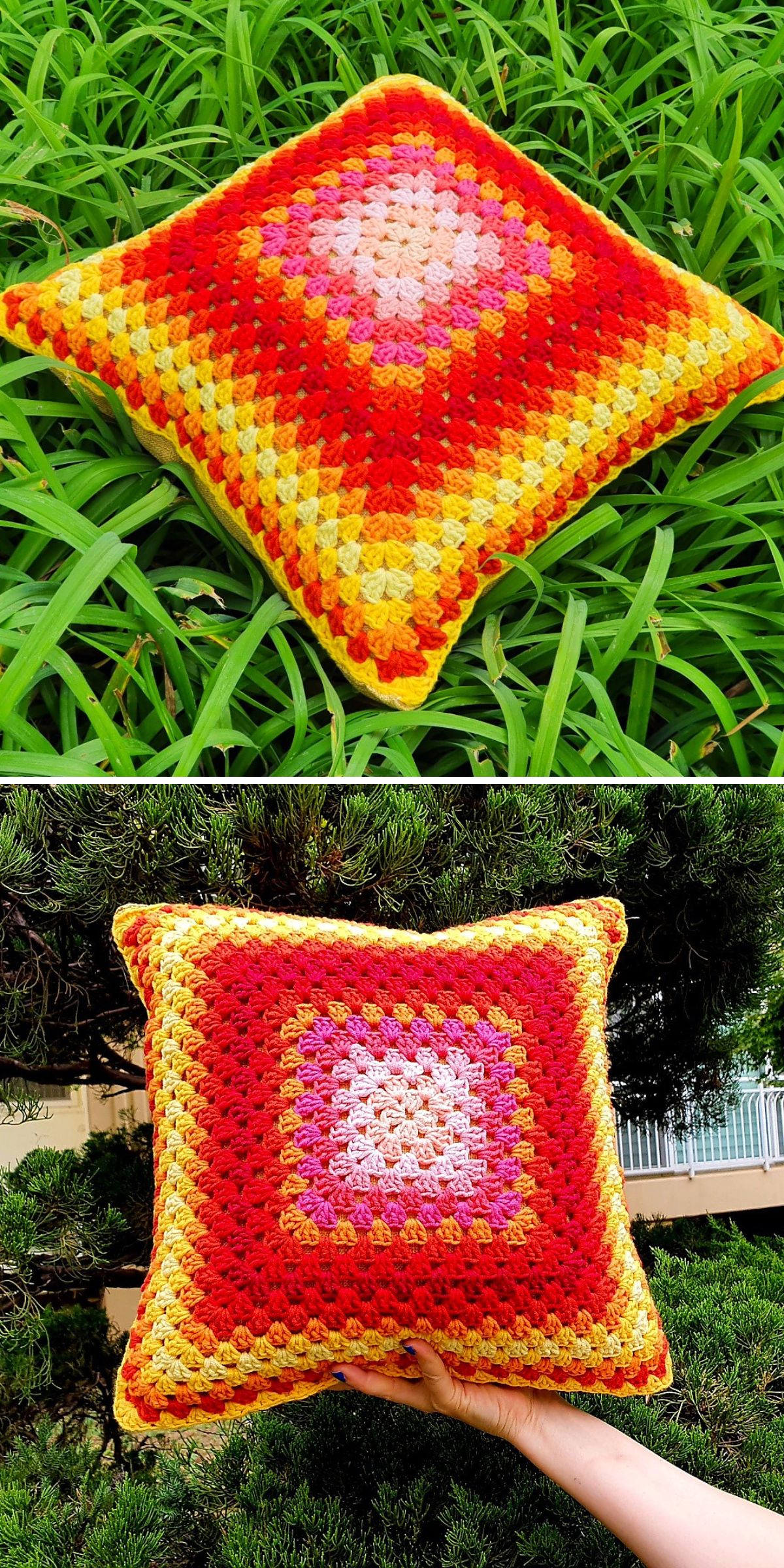 A crocheted geometric pillow with a vibrant red, pink, and yellow pattern is displayed on grass and held in front of a tree.