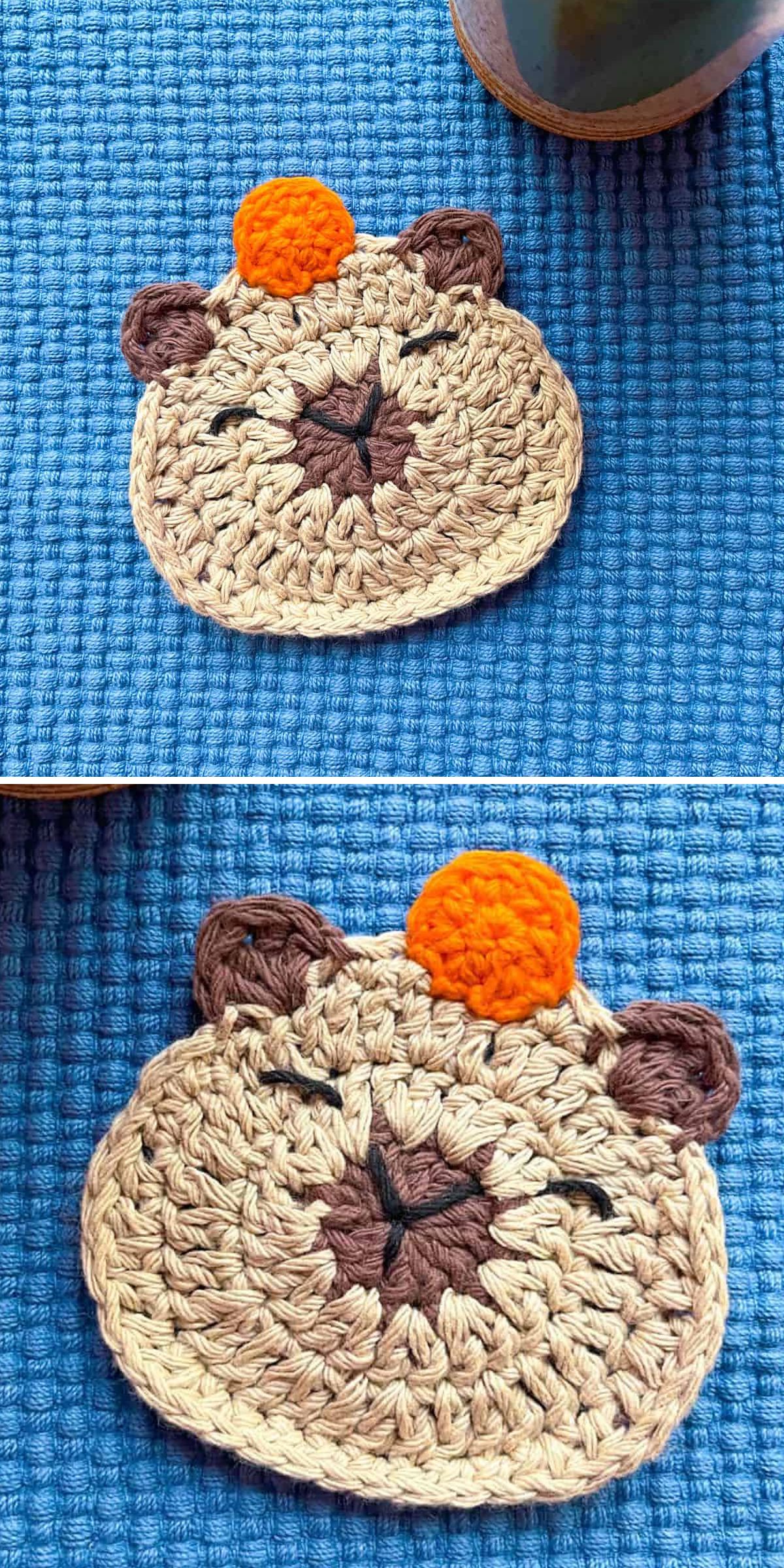 A crochet capybara face with closed eyes, brown ears, and an orange circle on its head sits on a textured blue surface.