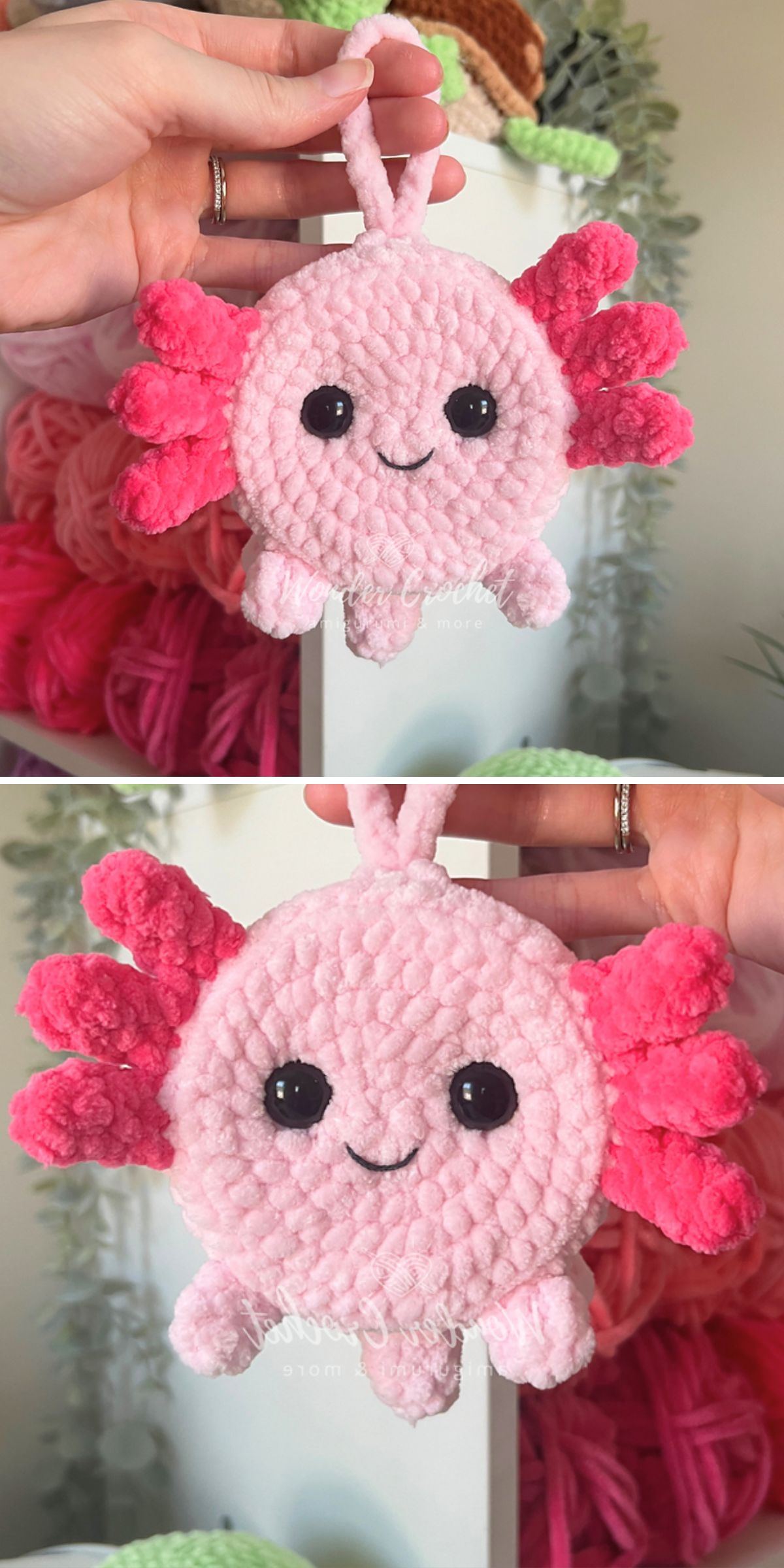 A hand holds a charming crochet axolotl plushie with bright pink gills, black button eyes, and a smiling mouth, set against a cozy background of yarn and plants.