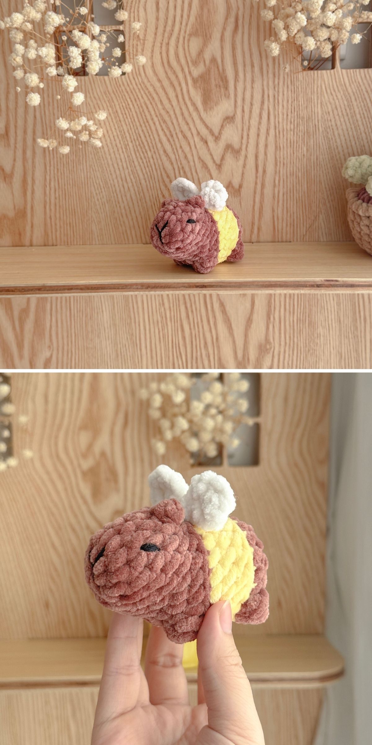 A small handmade plush toy resembling a bee with a brown head, yellow body, and white wings sits on a wooden shelf and is held up for closer view, accompanied by an adorable crochet capybara for an extra touch of charm.