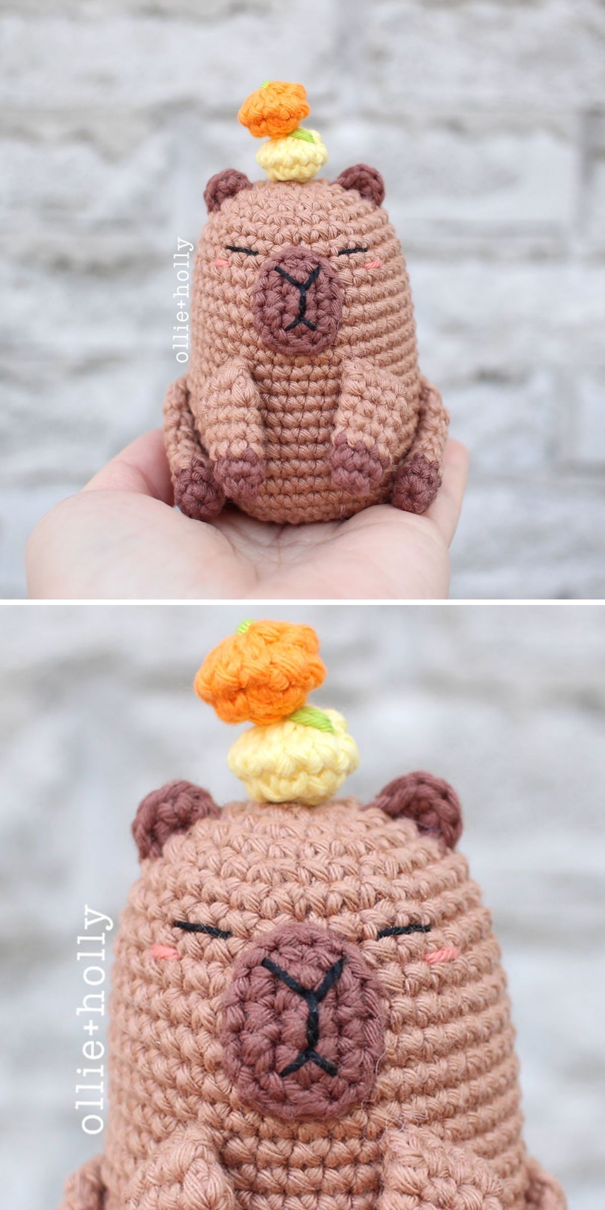 A hand holds a crochet capybara with closed eyes and a crocheted orange-yellow citrus fruit resting on its head. The background features a light gray brick wall.