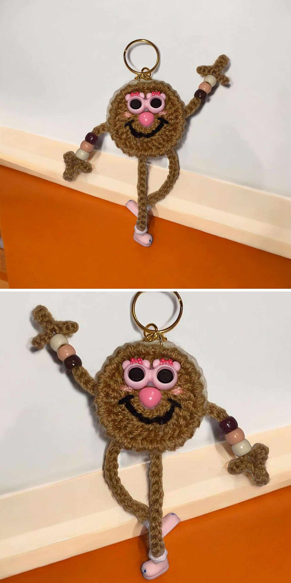 A charming crochet keychain figure with pink glasses, a nose, and yarn-crafted arms and legs accented by beads, displayed on an orange and white surface.