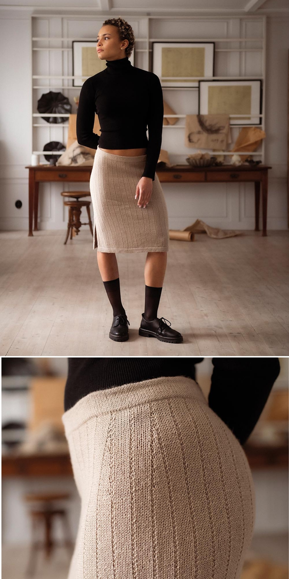 A person wears a black turtleneck, beige knit skirt with ribbed detailing, black socks, and shoes, standing in a bright, minimalist room with art and books displayed in the background.