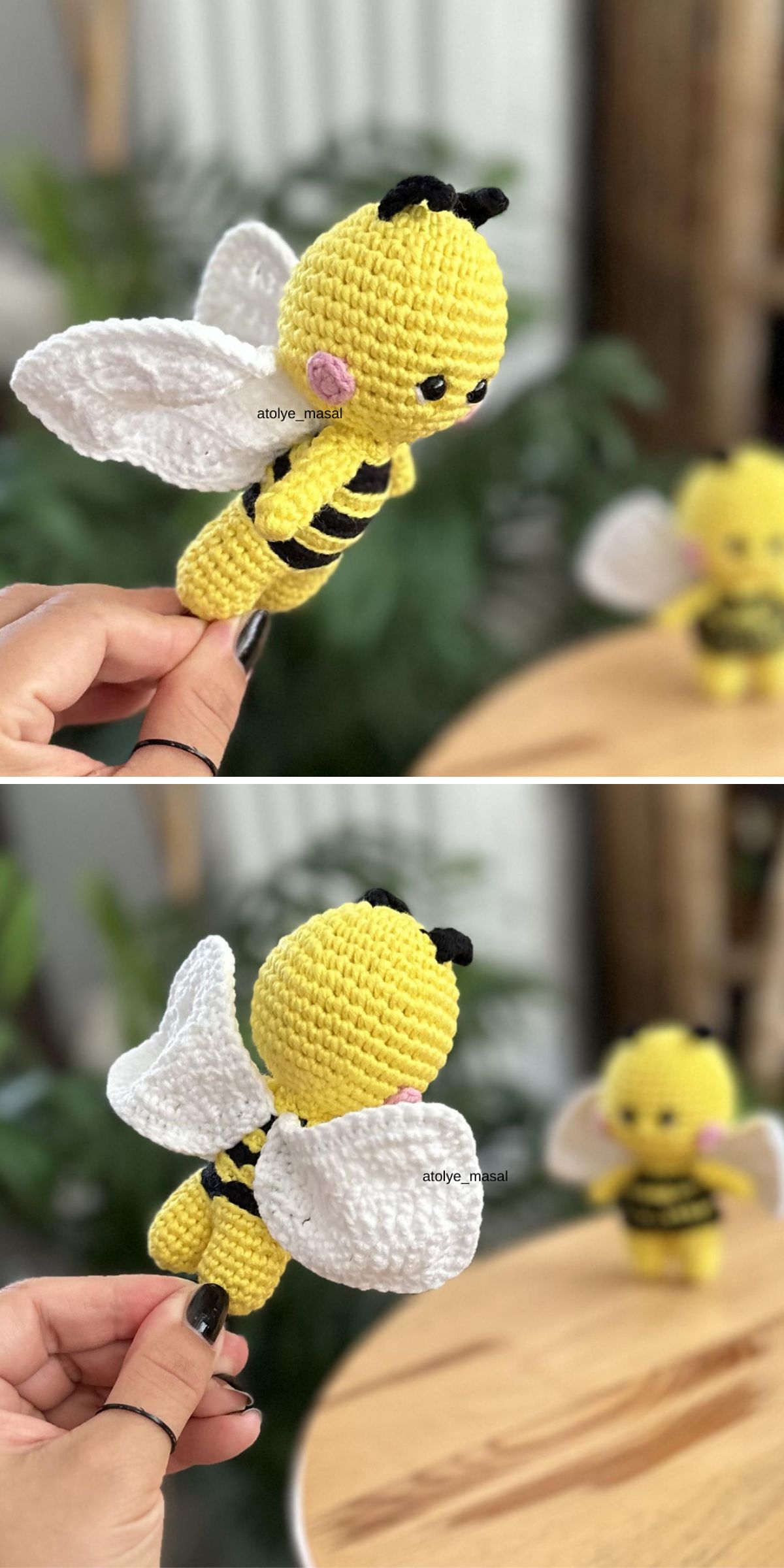 Hand holding a crocheted bee toy with white wings; another similar bee toy is blurred in the background on a wooden surface.