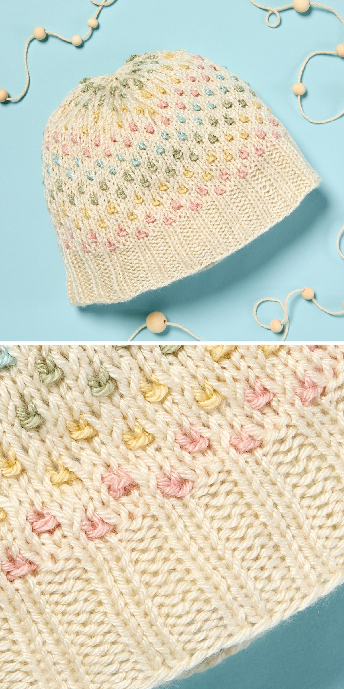 A knitted hat in a soft cream color features a ribbed brim and pastel-colored bobble accents, beautifully displayed on a light blue background with wooden beads and string.